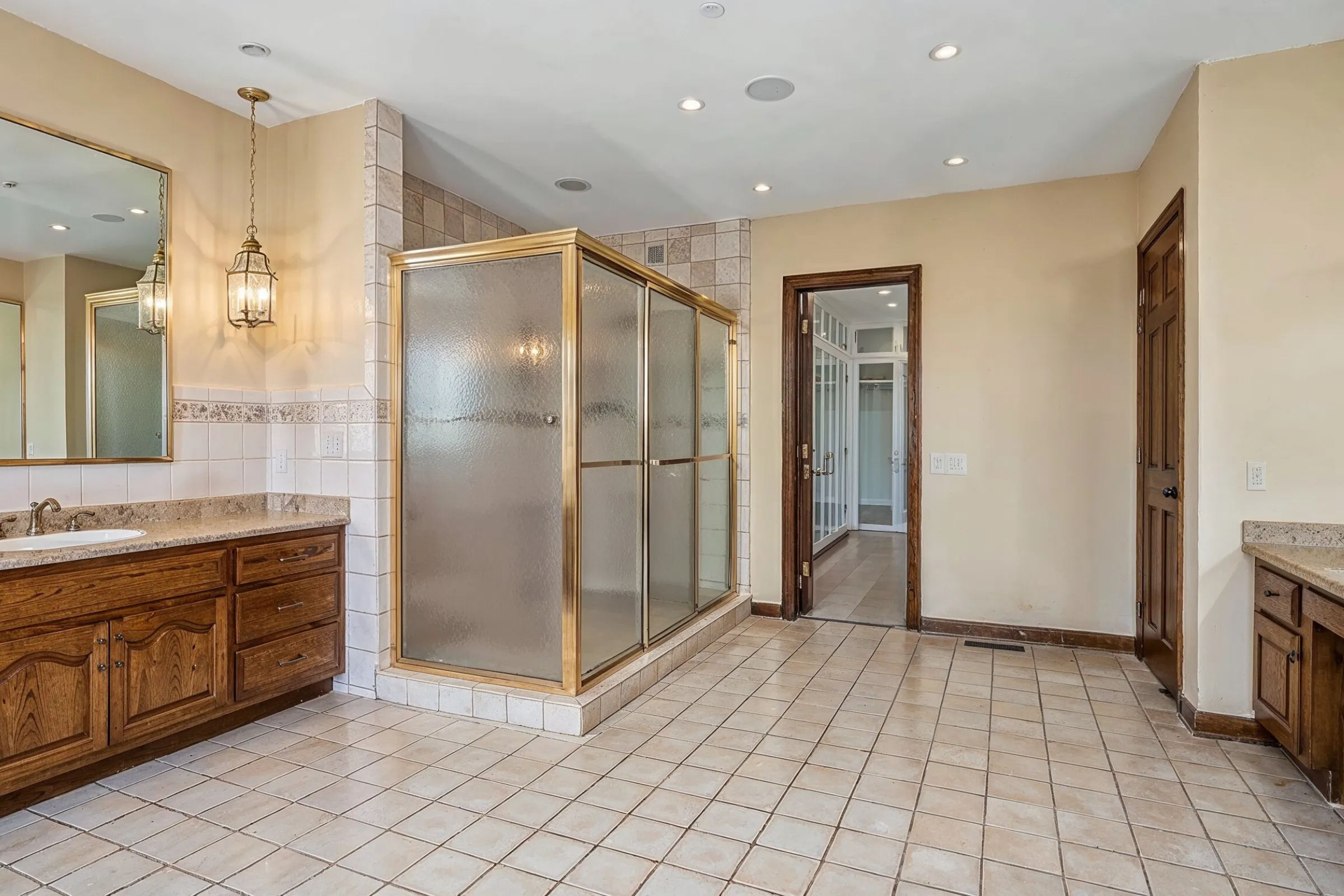 Before bathroom remodeling project in Los Angeles showing outdated tile shower, older vanity cabinets, dated flooring, brass shower frame, poor lighting, and worn bathroom finishes
