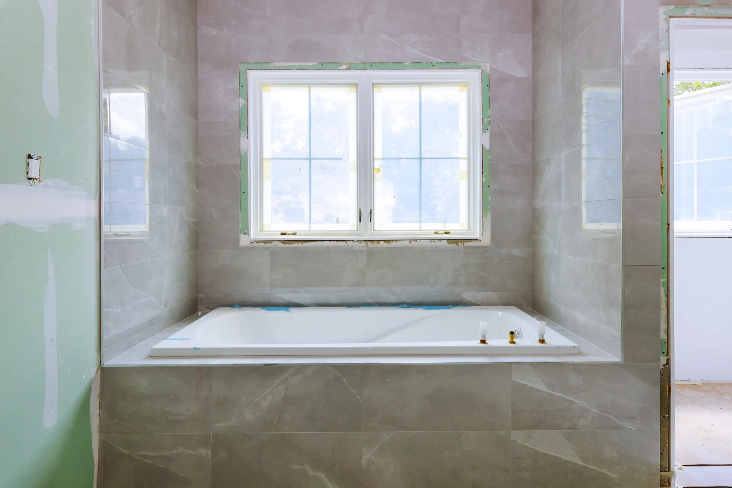 Bathroom remodeling in Los Angeles with bathtub installation, large-format wall tile, window trim preparation, and shower surround renovation in progress